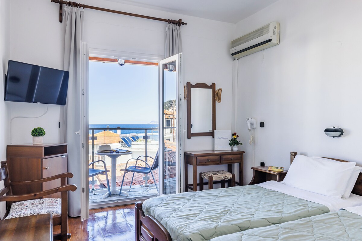 Habitación de hotel con cama, escritorio, silla, televisor, aire acondicionado y balcón con vistas al mar.