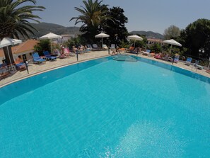 Una piscina con sillas de descanso y sombrillas, rodeada de palmeras y edificios.