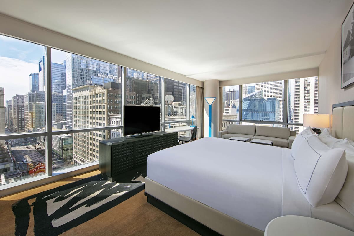 A hotel room with a large bed, a TV, a sofa, and a view of the cityscape.