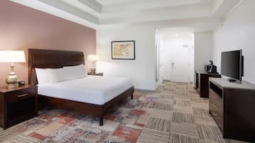 A hotel room with a large bed, a TV, a desk, and a patterned carpet.