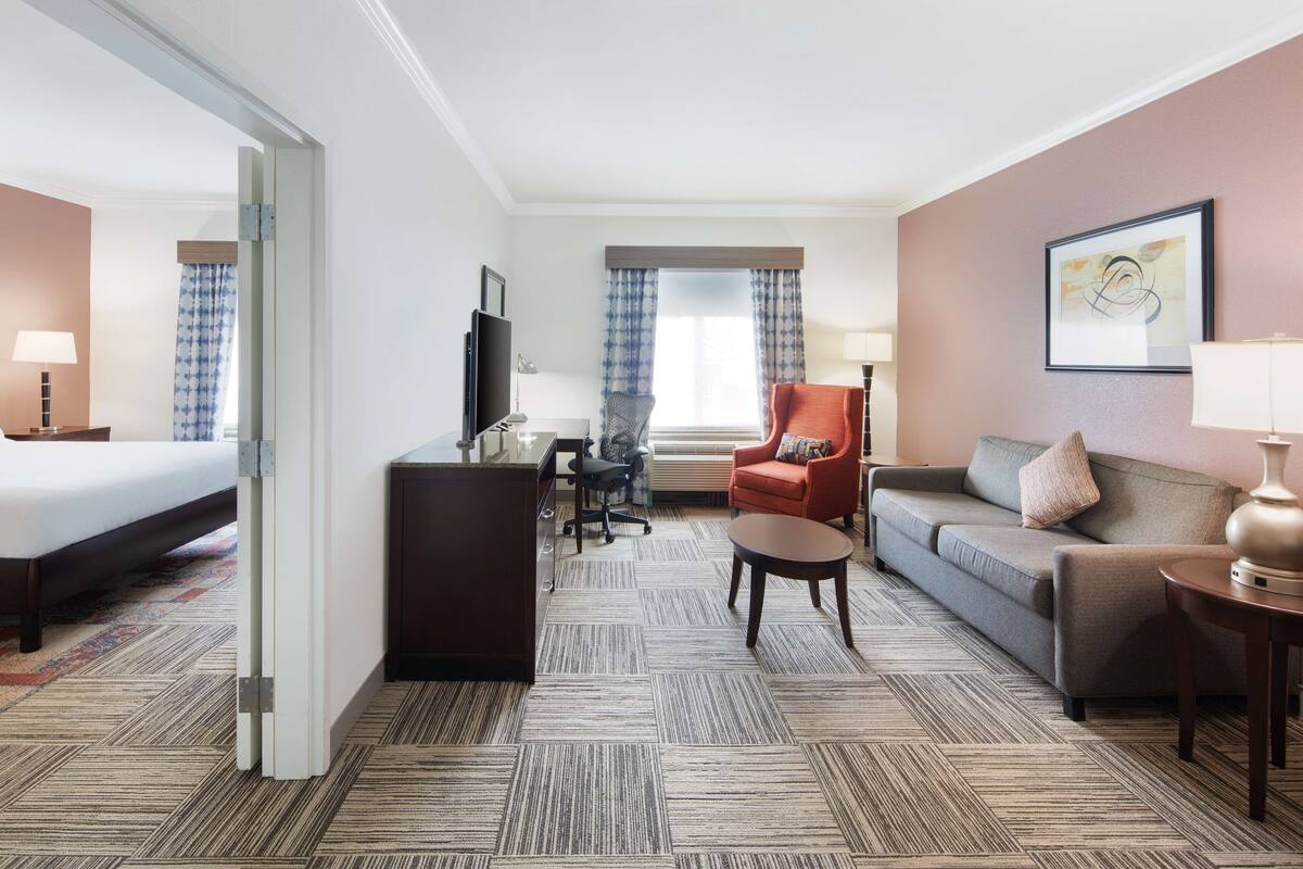A hotel room with a bed, a desk, a sofa, a chair, and a TV.