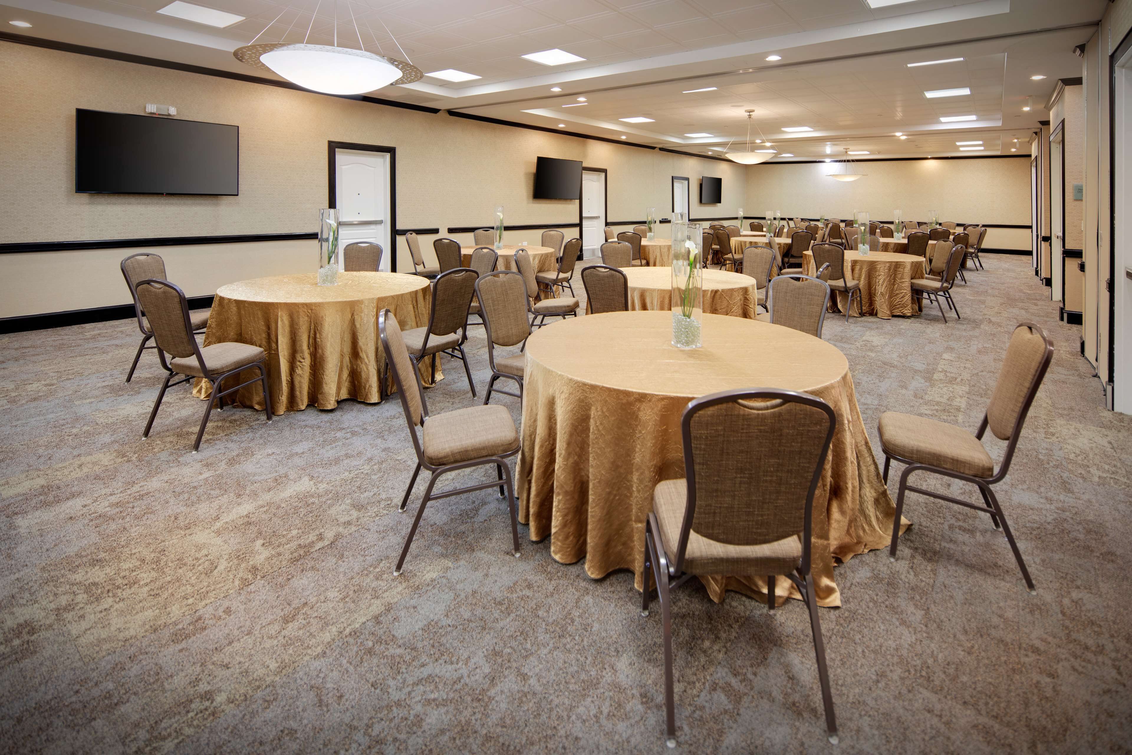 A conference room with multiple round tables, chairs, and a large flat-screen TV on the wall.