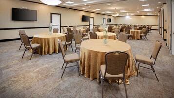 A conference room with multiple round tables, chairs, and a large flat-screen TV on the wall.