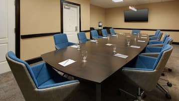 A conference room with a large table, blue chairs, and a flat-screen TV on the wall.