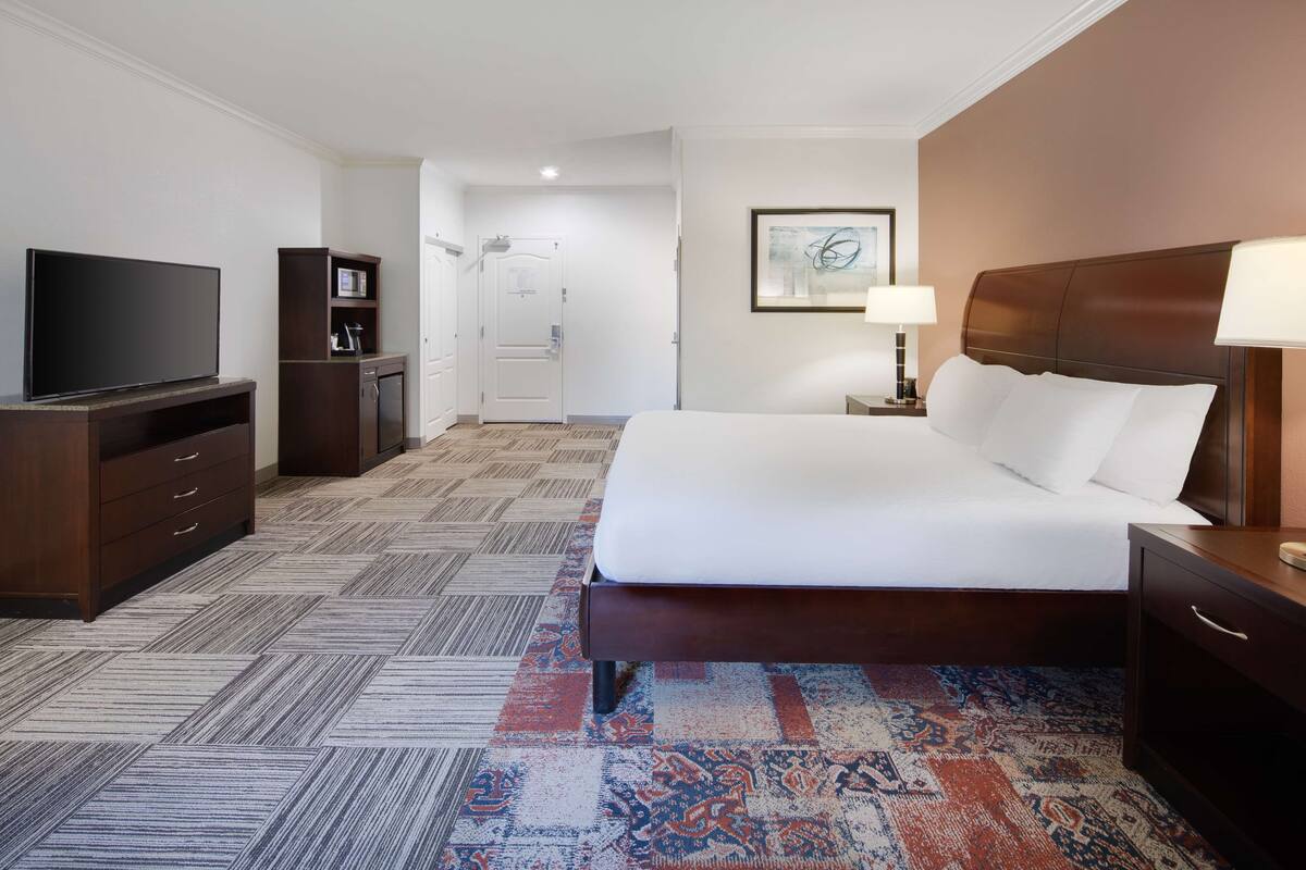 A hotel room with a large bed, a television, a desk, and a wardrobe.