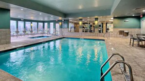 An indoor swimming pool with clear water, surrounded by a tiled floor and a glass barrier.