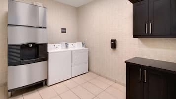A compact kitchen with a stainless steel refrigerator, a washing machine, and a dark wooden cabinet.