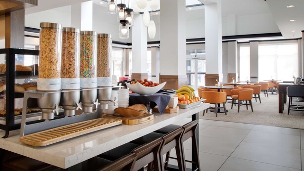 A breakfast bar with multiple beverage dispensers, a bowl of fruit, and a variety of breakfast items.