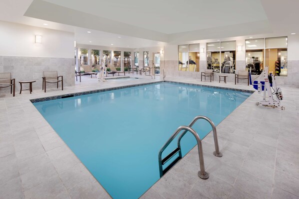 A large indoor swimming pool with a tiled floor, surrounded by lounge chairs and exercise equipment.