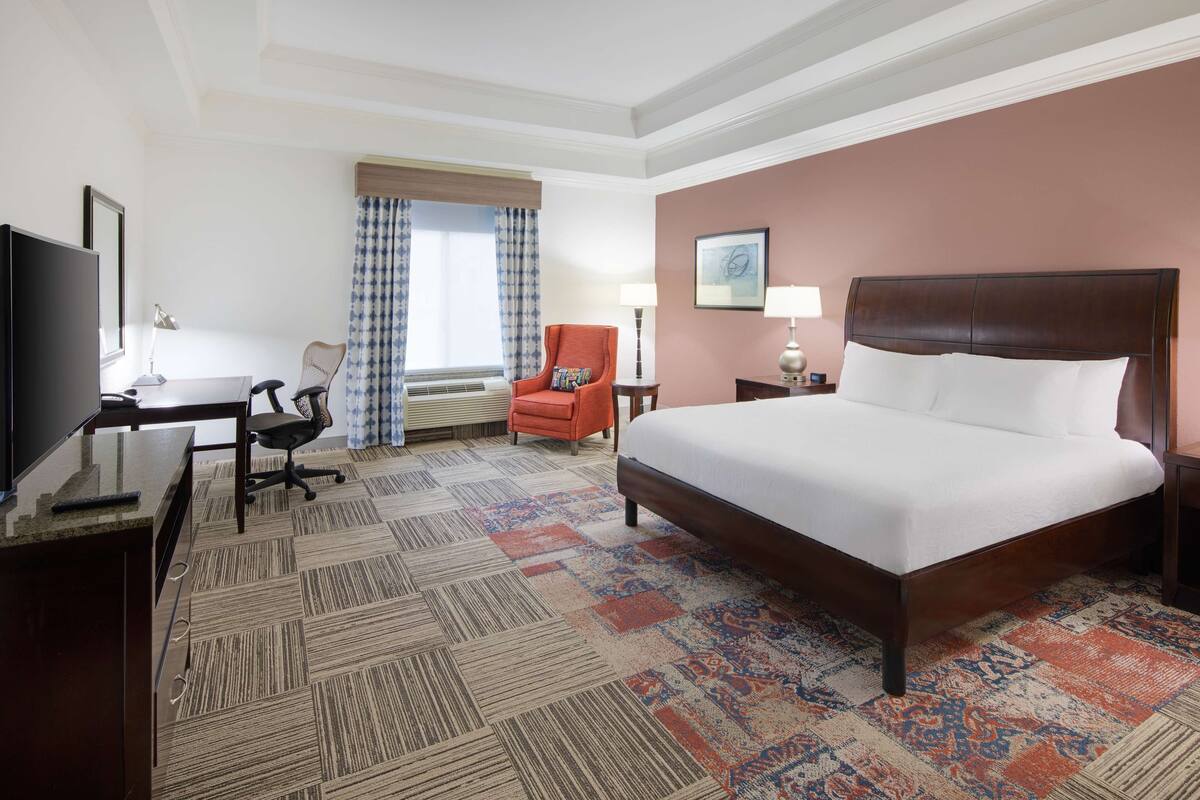 A hotel room with a large bed, a desk with a chair, a television, and a window with curtains.