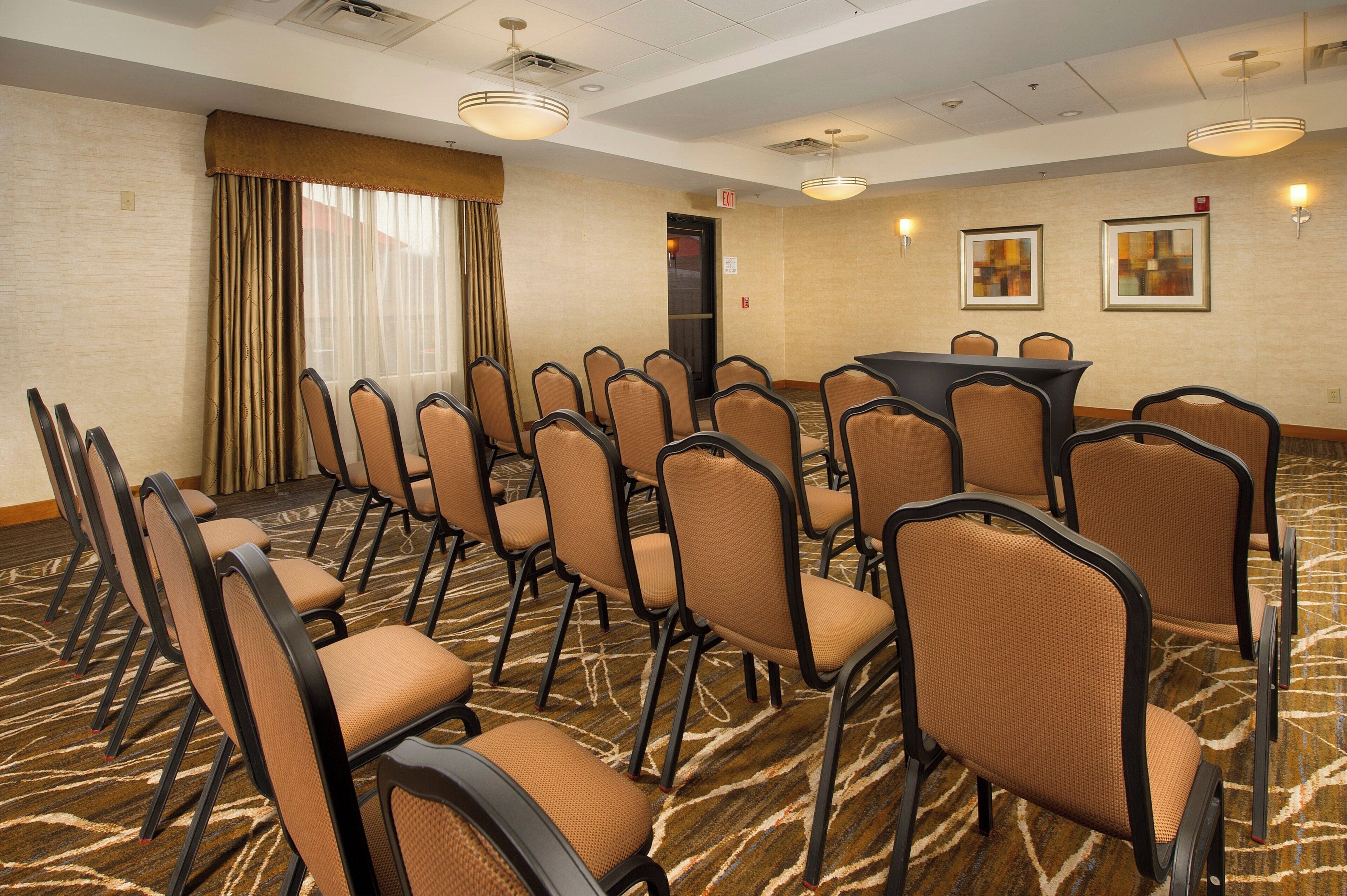 A conference room with rows of chairs, a table, and two exit signs on the wall.