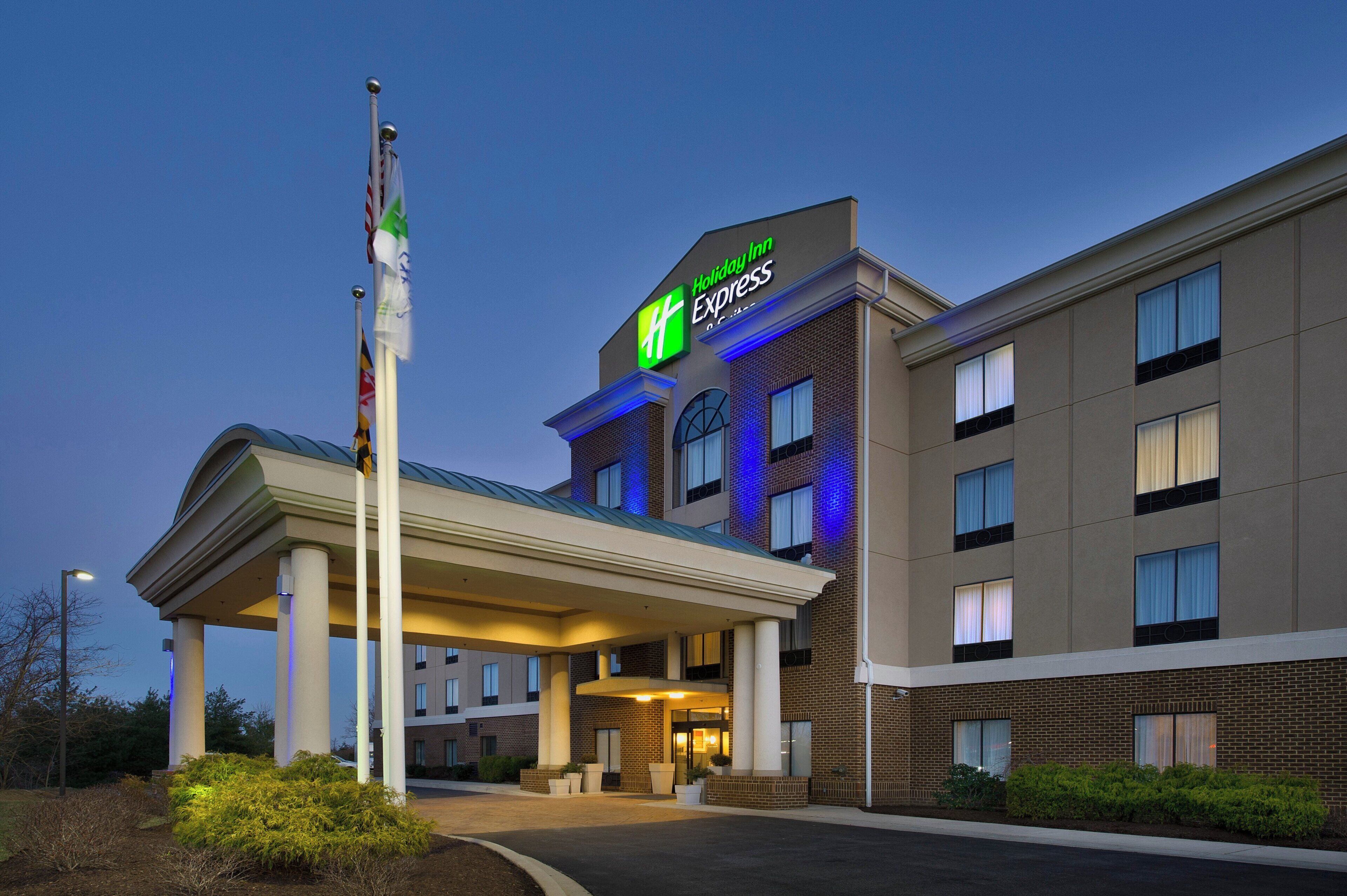 Un hotel Holiday Inn Express con entrada cubierta, varias ventanas e izado de banderas en un asta.