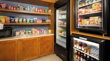 A kitchenette with a microwave, a refrigerator stocked with beverages, and shelves with snacks and condiments.