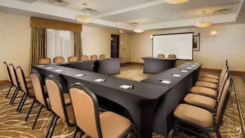 A conference room with a long table, chairs, a projector screen, and a carpeted floor.