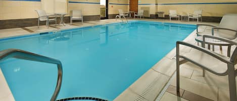 An indoor swimming pool with clear water, surrounded by lounge chairs and a tiled floor.