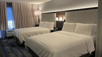Une chambre d’hôtel avec deux lits, une table de chevet, une lampe et une fenêtre avec des rideaux.