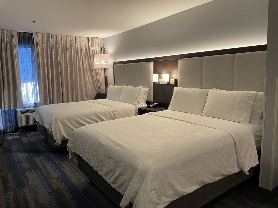 Une chambre d’hôtel avec deux lits, une table de chevet, une lampe et une fenêtre avec des rideaux.