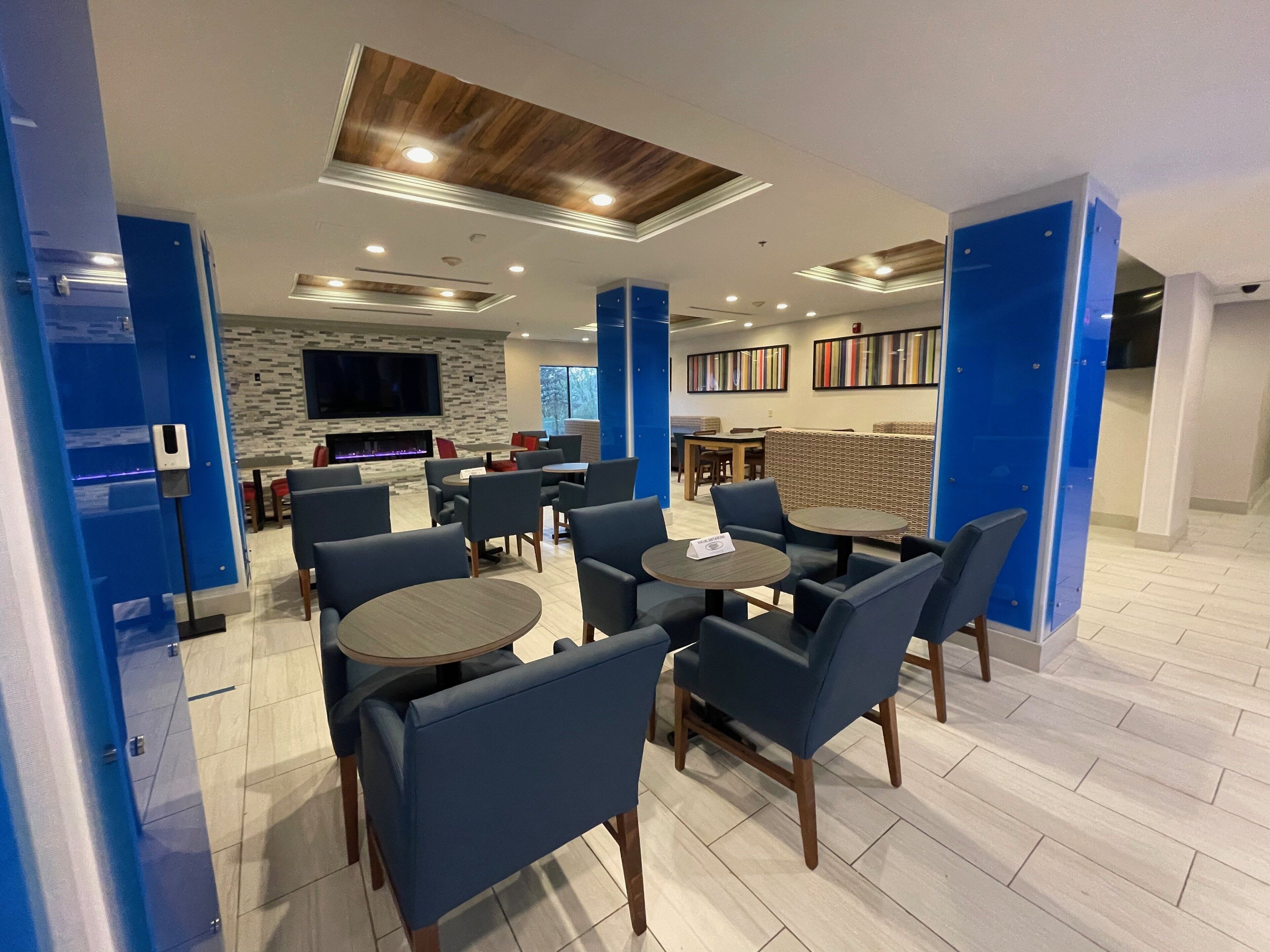 A modern indoor seating area with round tables and blue chairs, a flat-screen TV, and a fireplace.