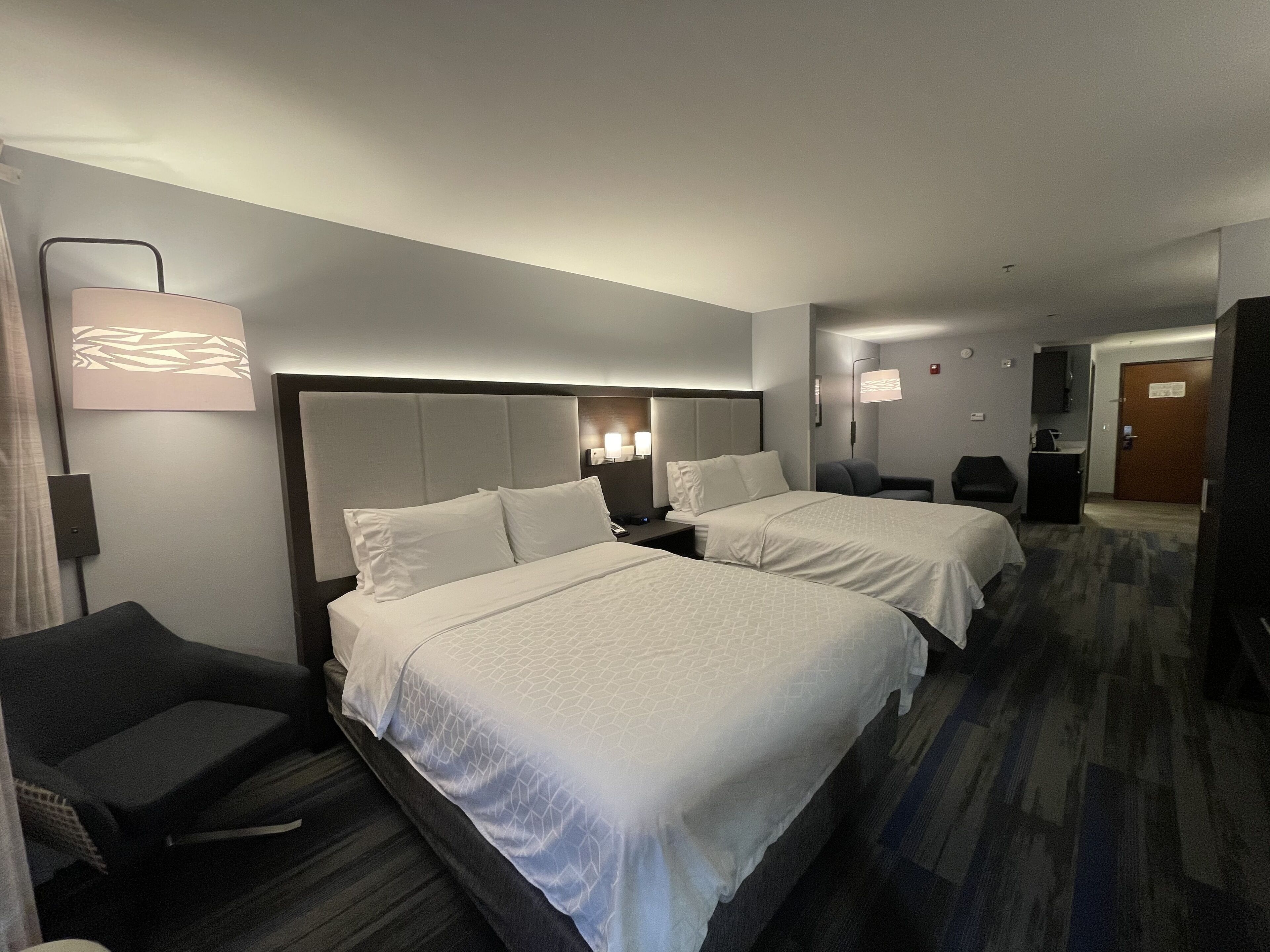 Et hotelværelse med to senge, et skrivebord, en stol, en lampe og et spejl.