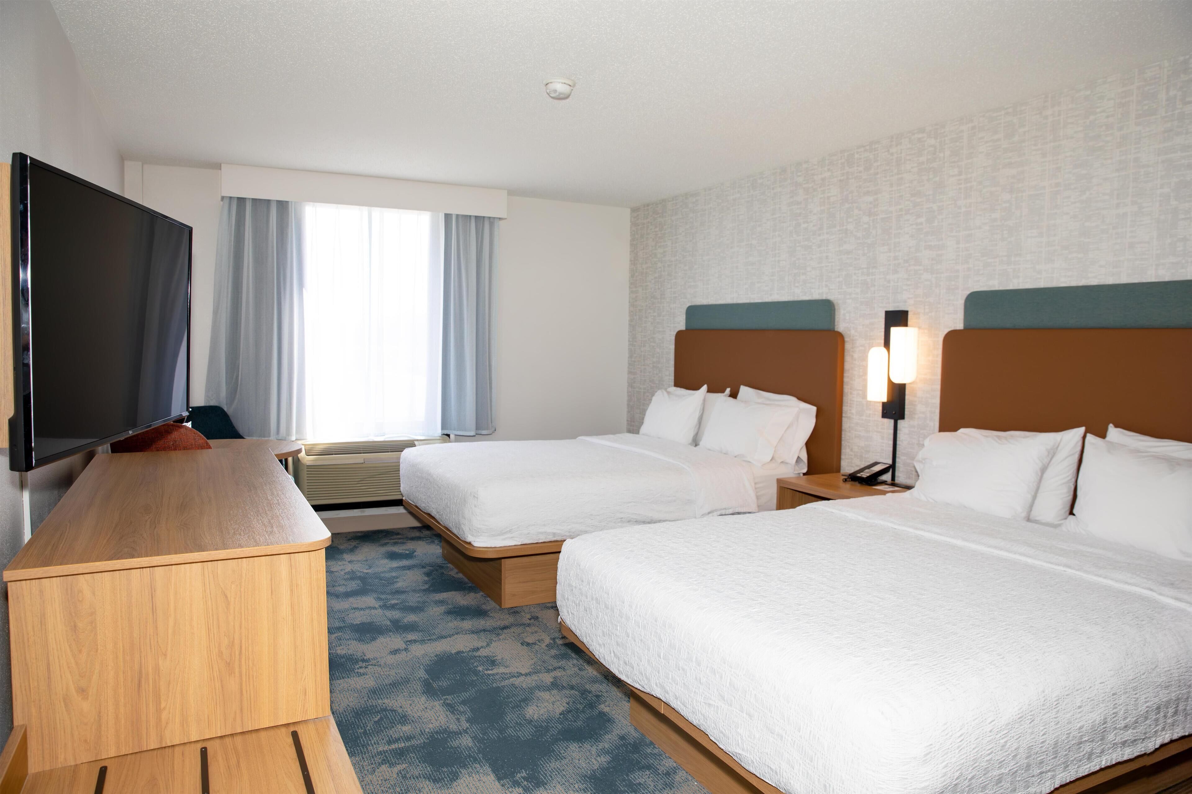 Habitación de hotel con dos camas, un escritorio, televisor y ventana con cortinas.