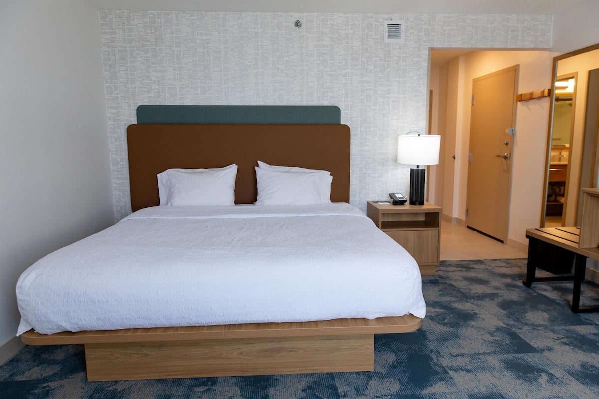 A hotel room with a large bed, a bedside table with a lamp, and a mirror on the wall.