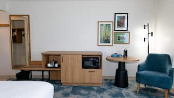 Una camera d'albergo con un letto, una scrivania con un forno a microonde, una sedia e un tavolino con una lampada. Alle pareti sono presenti quadri incorniciati.