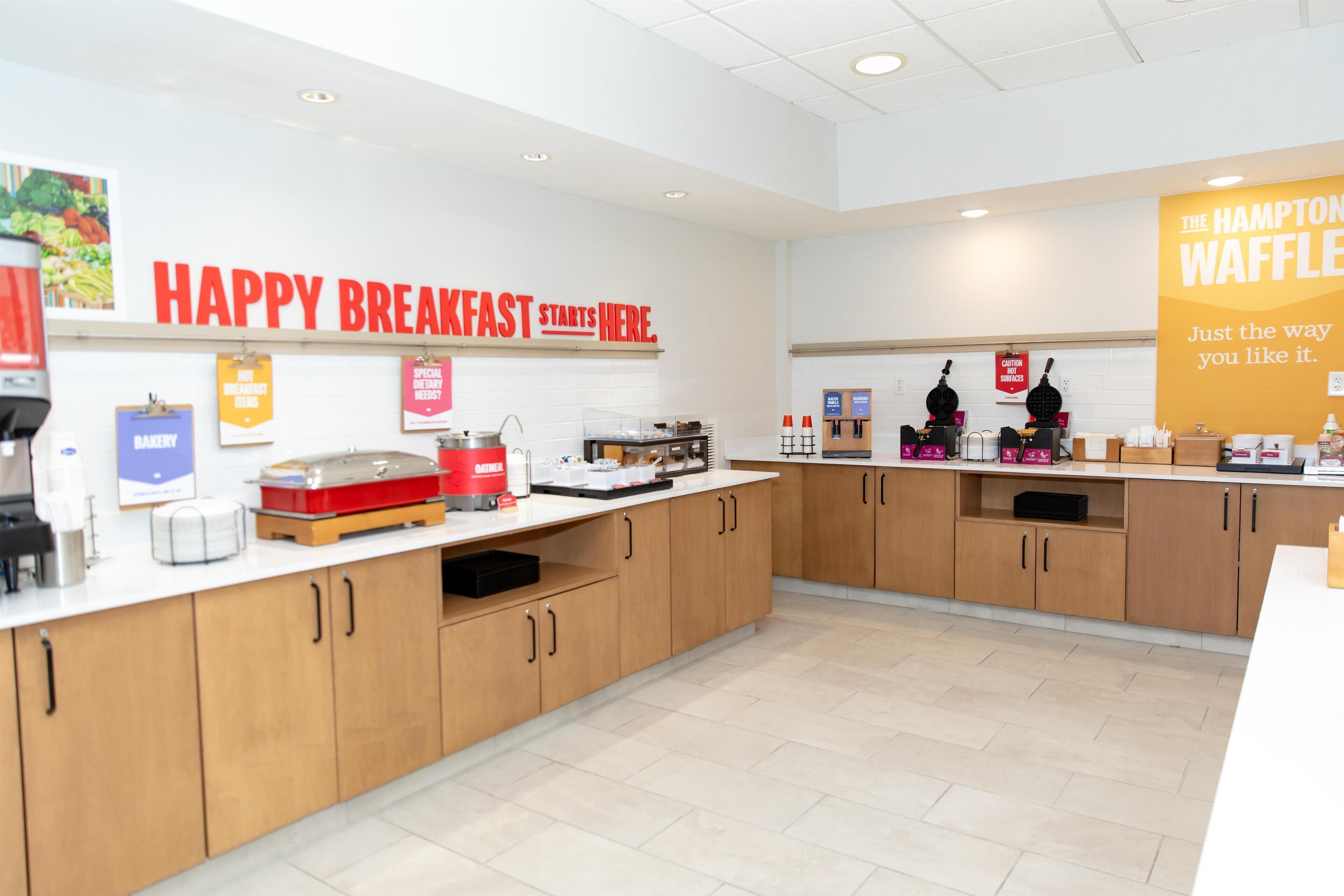 A breakfast area with a counter displaying various food items and a sign that reads "HAPPY BREAKFAST STARTS HERE."