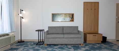 Una habitación con sofá gris, una mesita, una lámpara de pie, un cuadro y un armario.