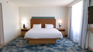 Une chambre d’hôtel avec un grand lit, deux tables de chevet avec des lampes, un téléviseur à écran plat et une grande fenêtre avec des rideaux.