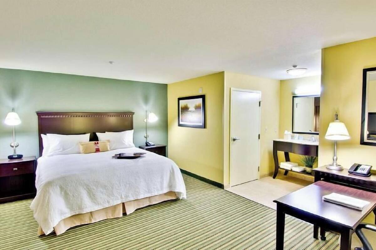 A hotel room with a large bed, bedside lamps, a desk, a chair, a mirror, and a door.