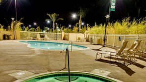 Un espace piscine nocturne comprenant un jacuzzi, des chaises longues et une clôture.