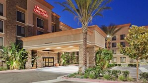 Un hôtel Hampton Inn & Suites doté d’une façade moderne, d’une entrée abritée et de palmiers.