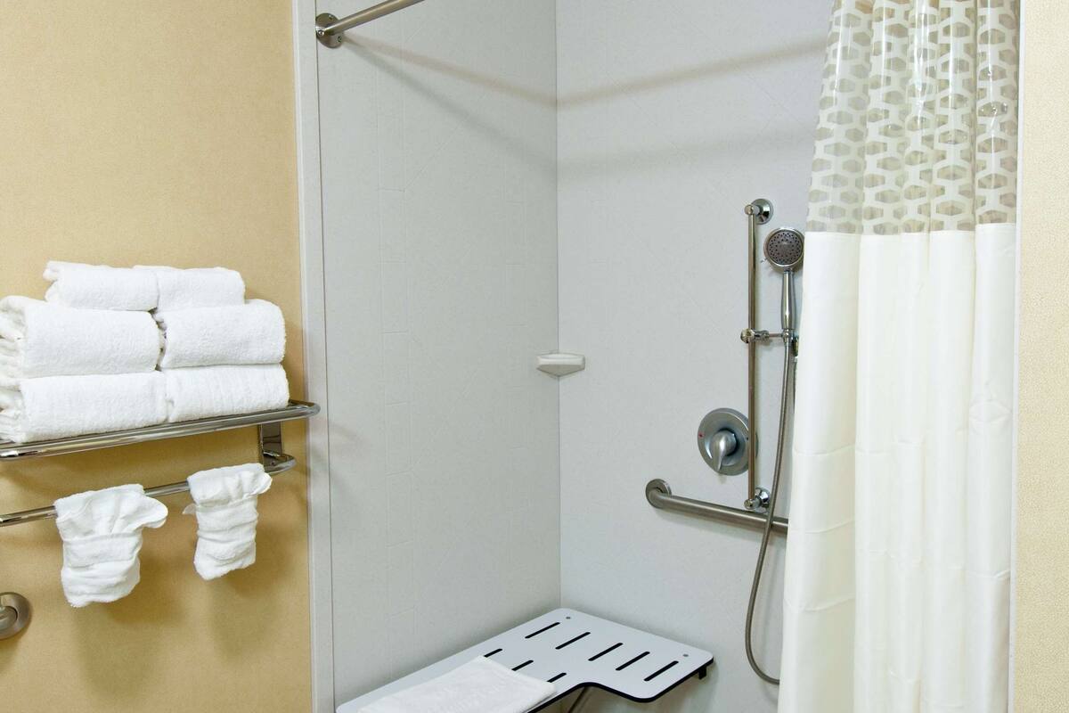 A shower area with a glass door, a towel rack with folded towels, a showerhead, and a shower curtain.