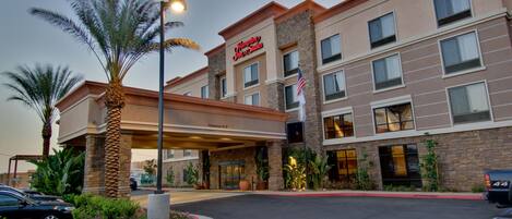 Un hôtel Hampton Inn avec une entrée bien visible, des palmiers et un parking.