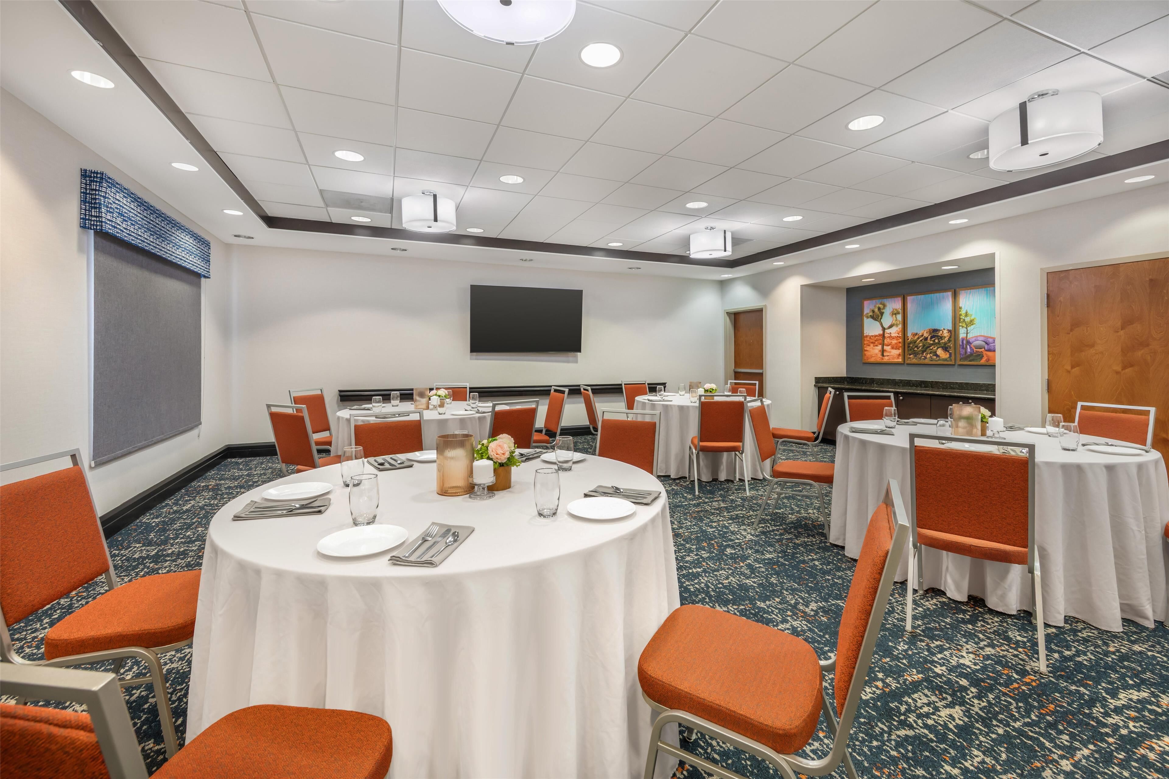 Une salle de conférence avec des tables rondes, des chaises orange et un grand écran.