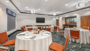 Un salón de conferencias con mesas redondas, sillas naranjas y una pantalla grande.