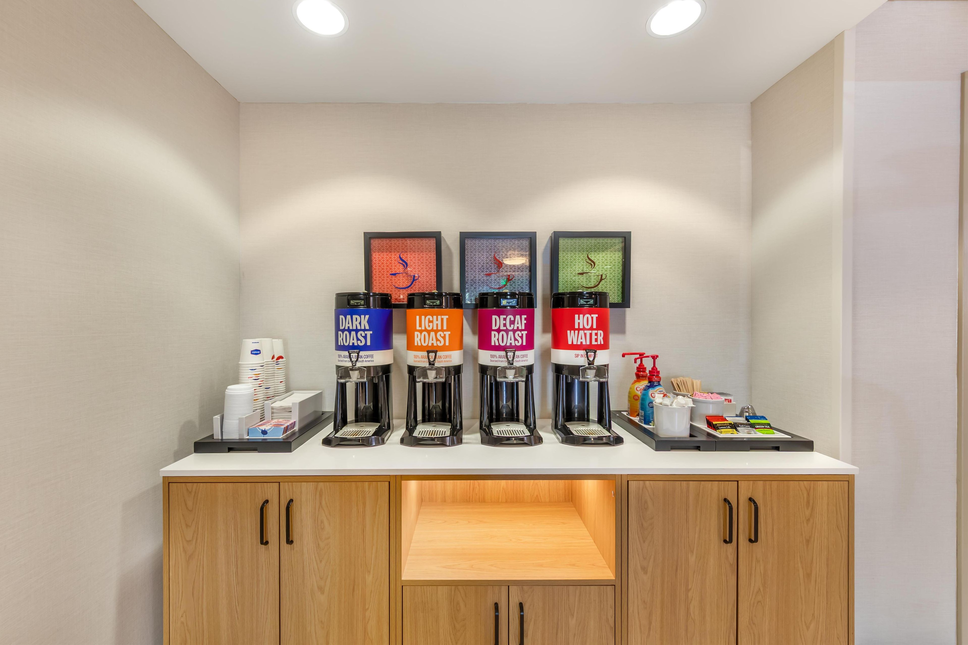 A coffee station with four dispensers labeled DARK ROAST, LIGHT ROAST, DECA ROAST, and HOT WATER.