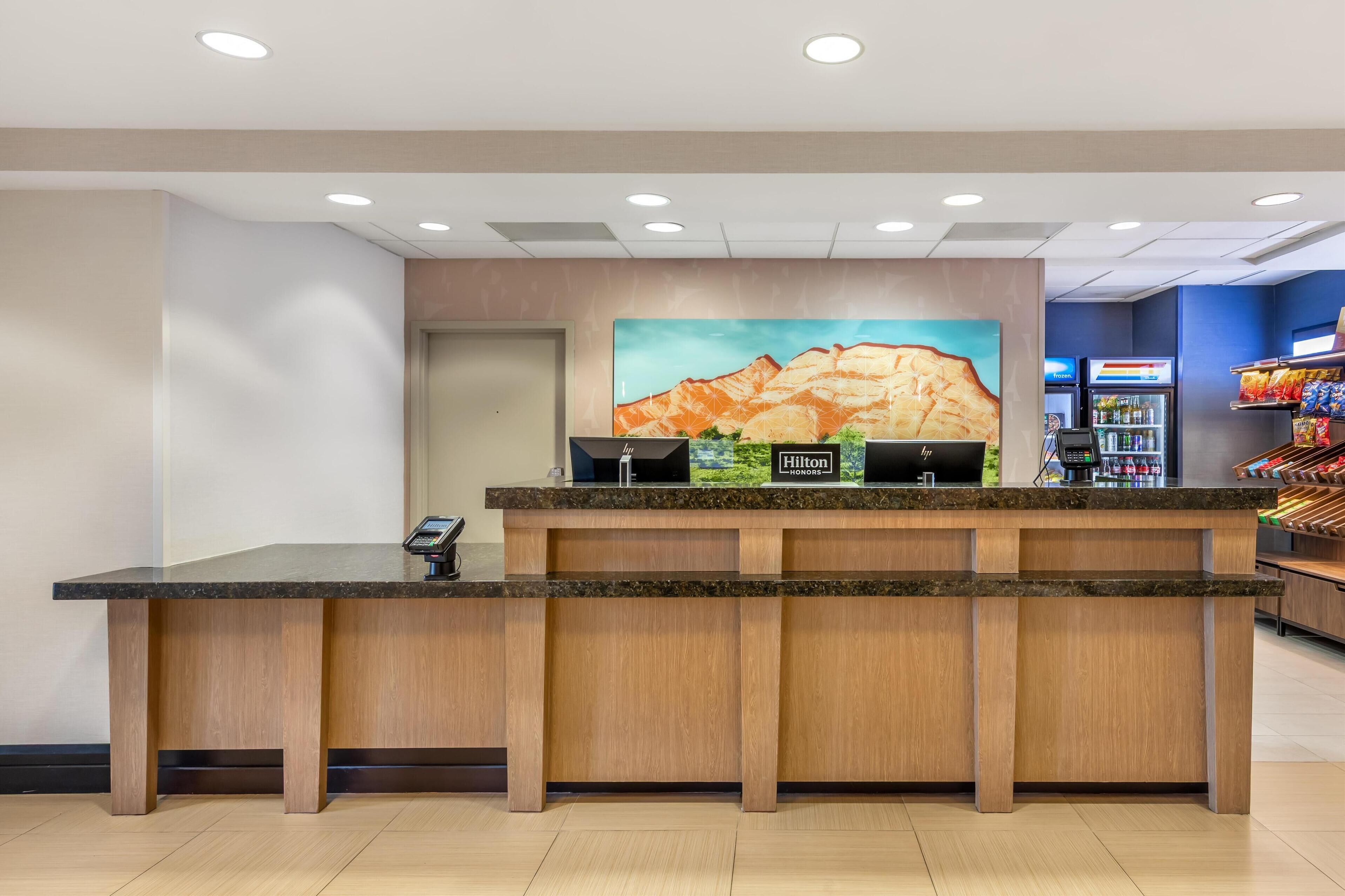 Un comptoir d’accueil d’hôtel agrémenté d’un tableau représentant des montagnes, un minibar et un espace proposant des boissons en libre-service.