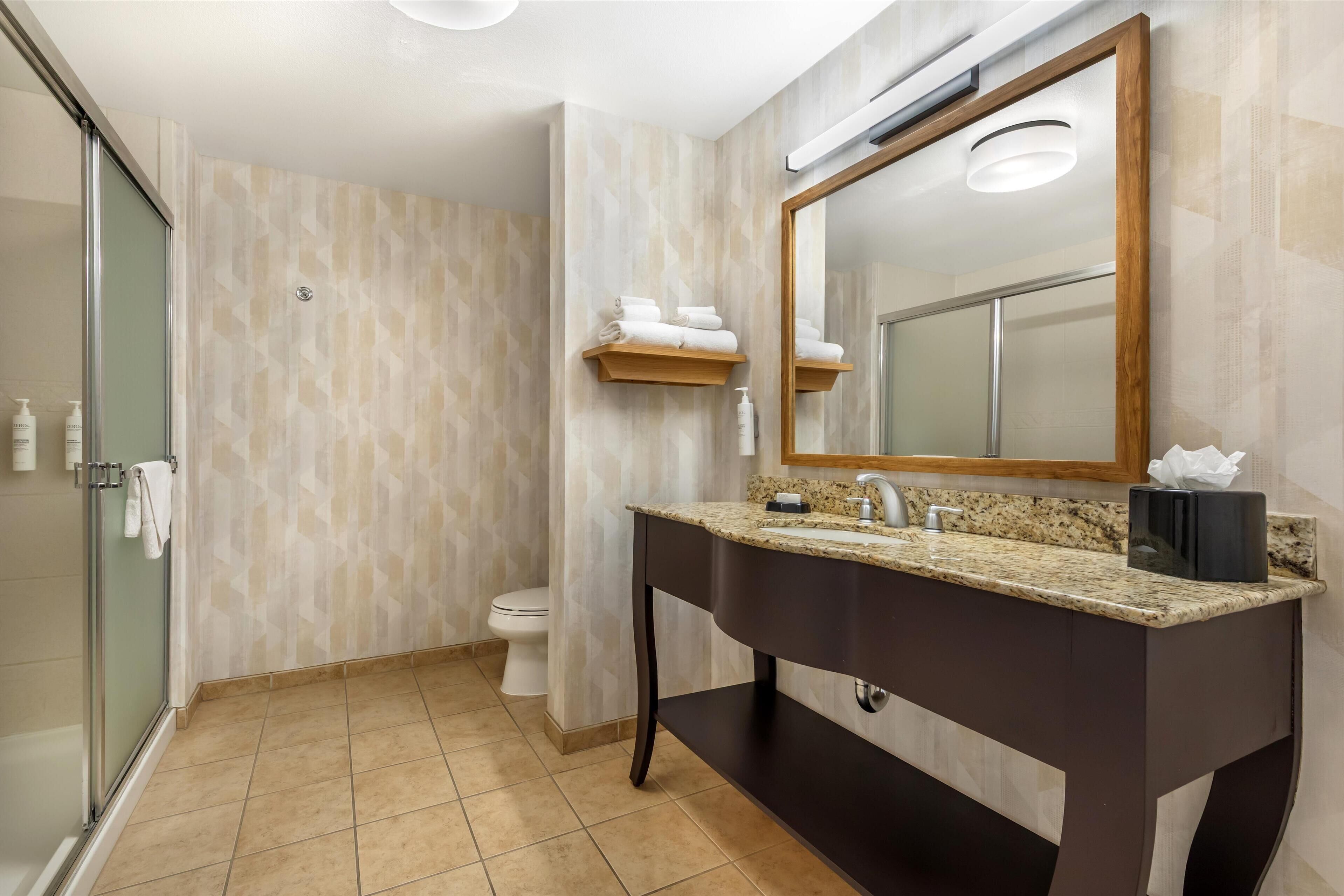 A modern bathroom with a glass shower enclosure, a dark vanity with a granite countertop, and a large mirror.