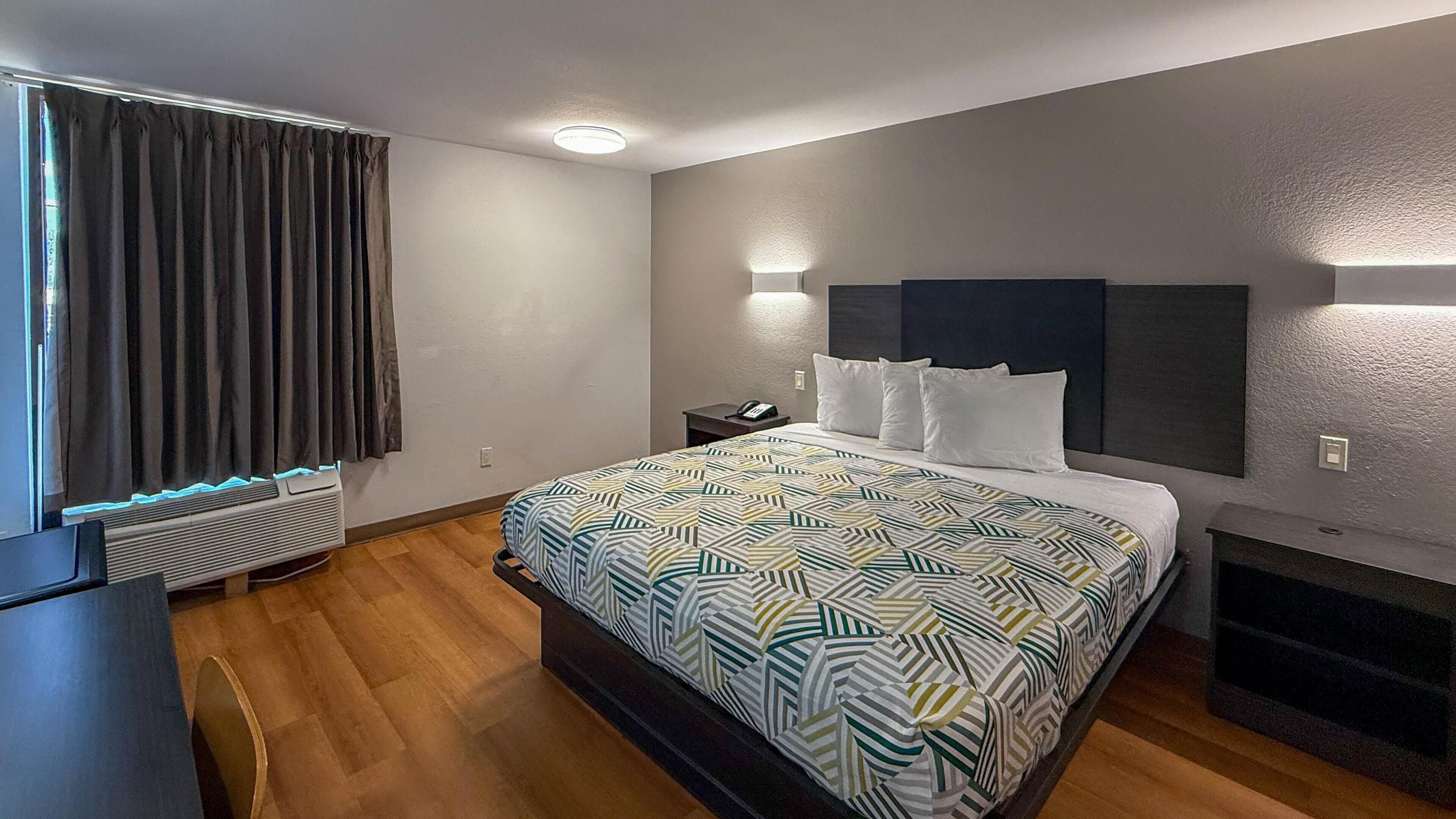 Ein modernes Hotelzimmer mit einem großen Bett, einem Nachttisch, einem Schreibtisch und einem fest installierten Fernseher.