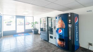 Un espace équipé de distributeurs automatiques de boissons Pepsi, d’un tapis bleu portant le numéro 9 et d’une plante.