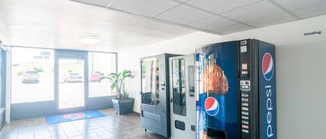Un espace équipé de distributeurs automatiques de boissons Pepsi, d’un tapis bleu portant le numéro 9 et d’une plante.