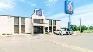 Un motel avec un grand panneau indiquant le chiffre « 6 », un parking où sont garées plusieurs voitures et un ciel d’un bleu éclatant.