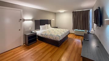 Habitación de hotel con cama, mesita de noche, lámpara, aire acondicionado y televisor montado en la pared.