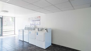 Une buanderie équipée de trois machines à laver, un plafond orné d’un motif en réseau et une porte donnant sur l’extérieur.