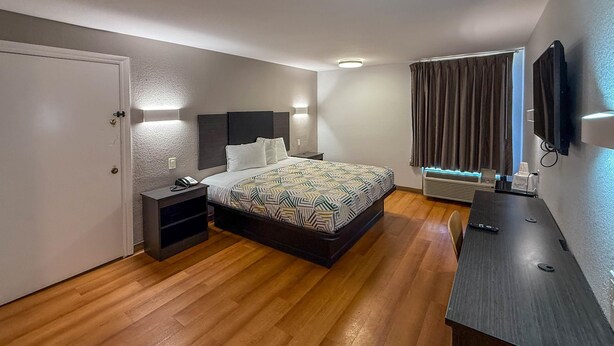 Une chambre d’hôtel avec un lit, des tables de chevet, un bureau, une télévision et une fenêtre avec des rideaux.