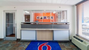 Un espace d’accueil avec une cloison en verre, un tapis bleu orné du chiffre 6 et une fenêtre avec des stores.