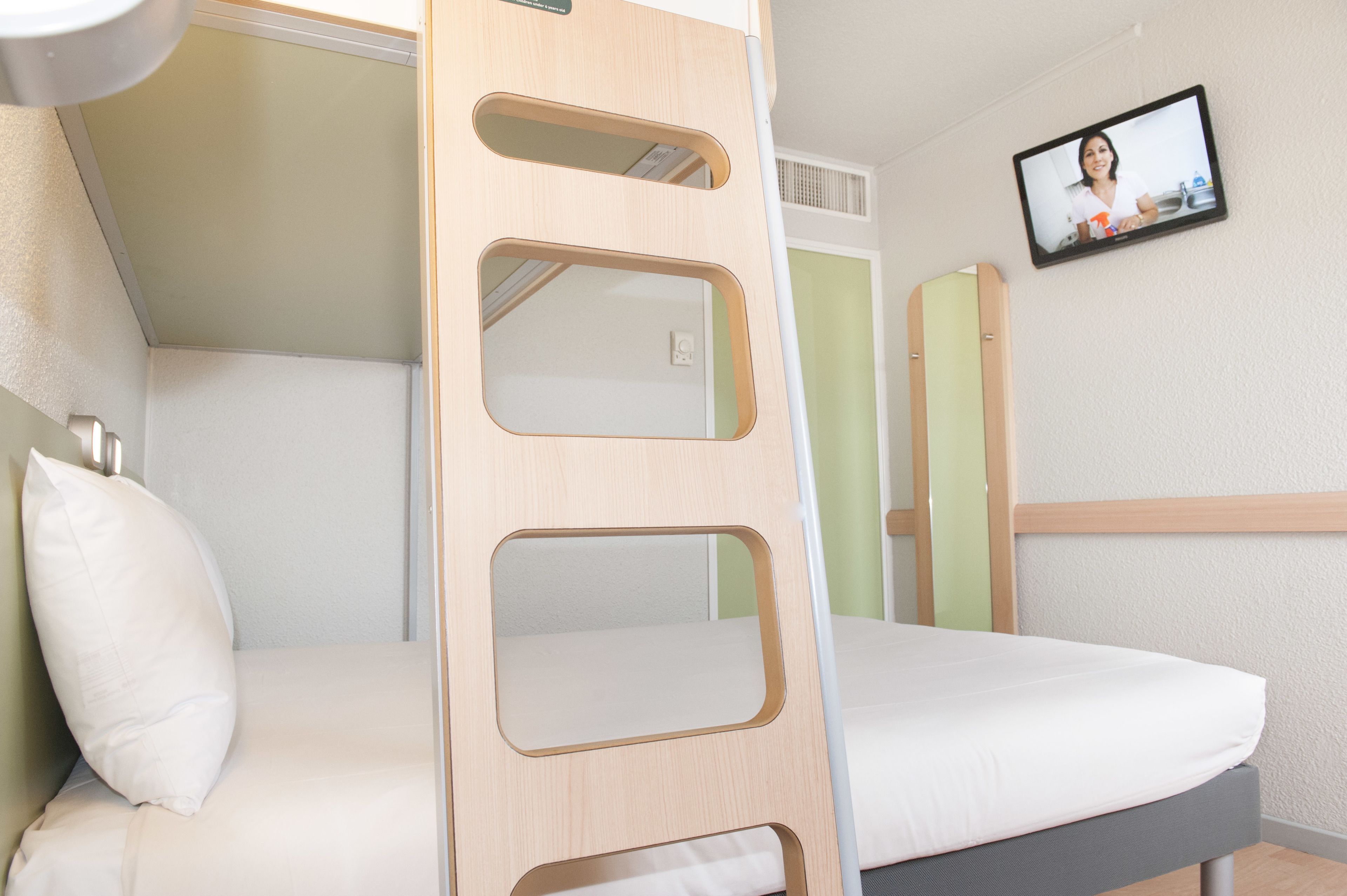 A bunk bed with a ladder, a television mounted on the wall, and a window.