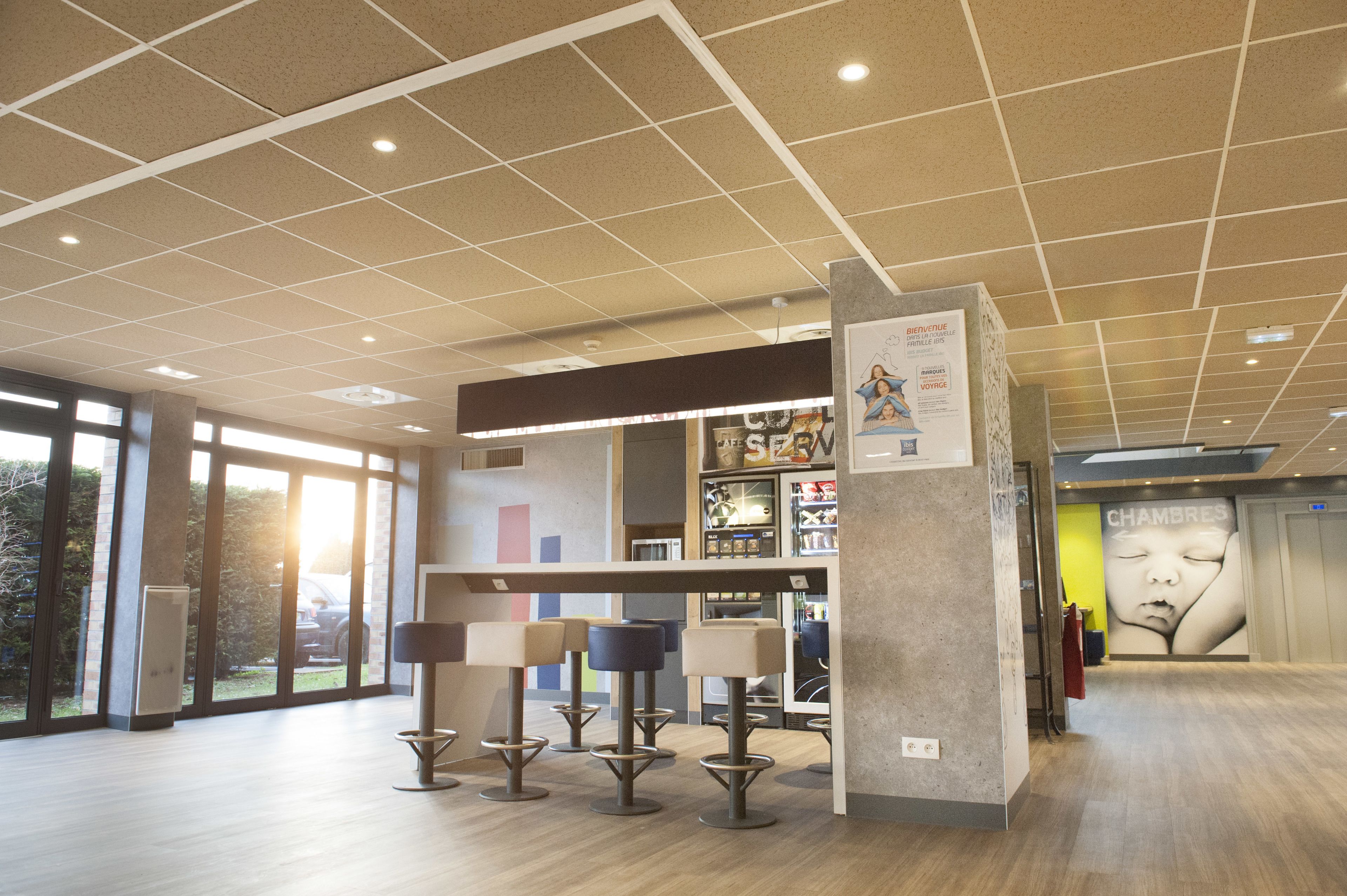 A modern interior with a high ceiling, large windows, and a central seating area with tables and chairs.