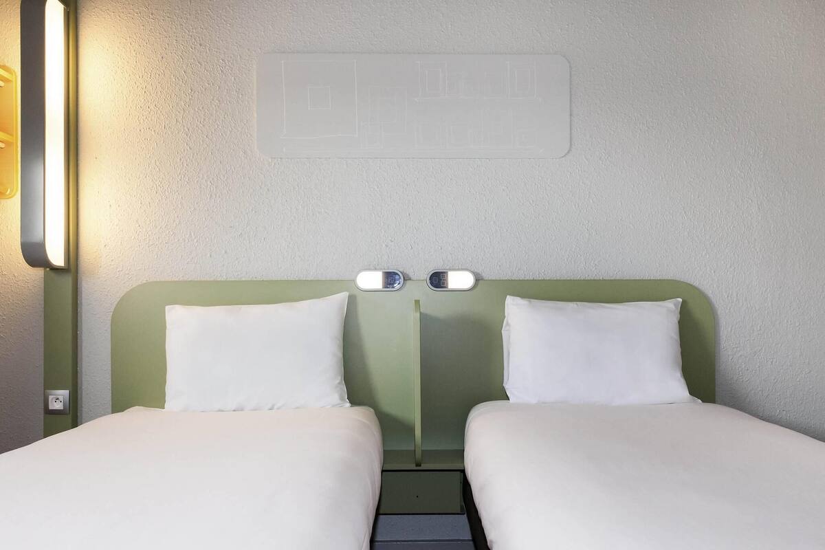A double room with two beds, a wall-mounted light, and a thermostat.